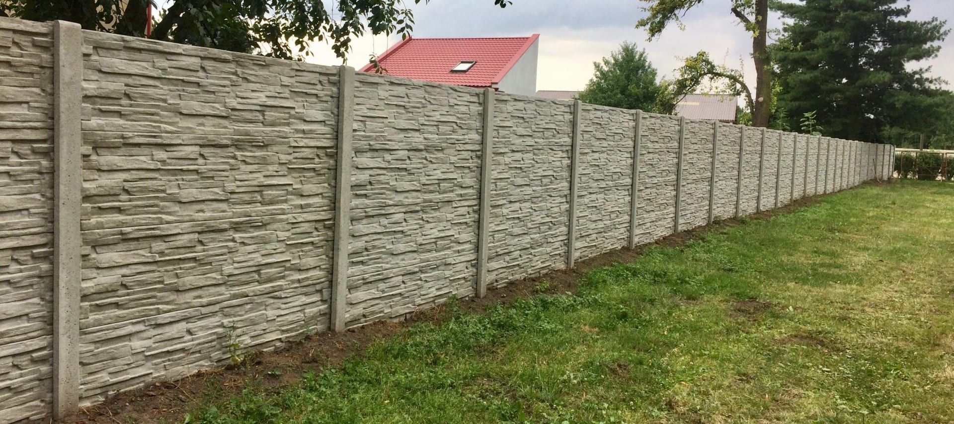 Betonový plot u rodinného domu s červenou střechou