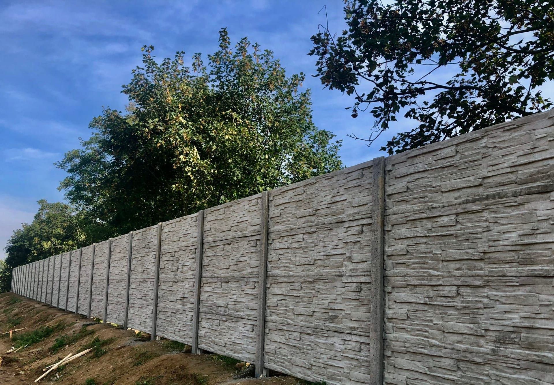 Šedý betonový plot na svažitém pozemku — realizace Stavíme ploty